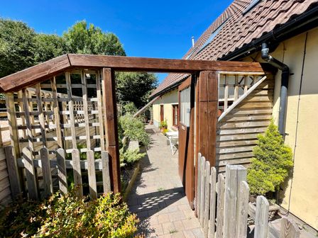 A wooden gate opening to a paved walkway beside a beige building with plants and wooden fencing surrounding the area at Mendip Cottage in Shipham