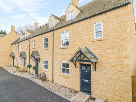 A row of stone houses with dark doors and small porches with benches and potted plants at Poets Corner in Bourton-On-The-Water