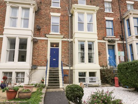 Front exterior of brick row houses with blue doors stairs and small garden areas at Abbey Vista in Whitby