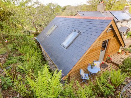A small wooden house with two skylights on the roof and a blue patio set on the wooden deck surrounded by greenery at Orchard Loft in Brownston near Modbury