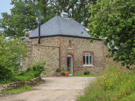 A stone house with a chimney and plants outside surrounded by trees and grass at The Old Laundry in North Tawton