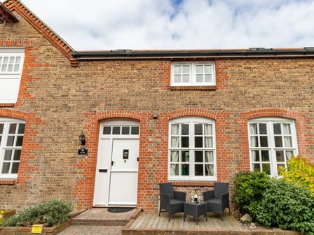 A brick house with white framed windows and door with two black chairs and a small table outside at Nuke in Weymouth