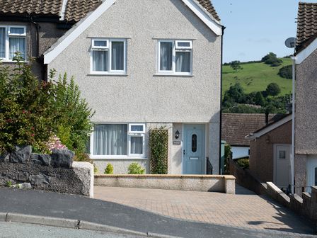 A front view of a semi detached house with a driveway and a green hill in the background at Heddfan in Conwy