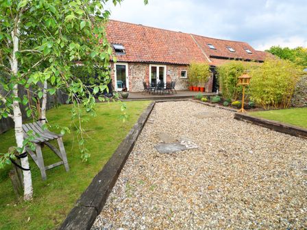 A garden with a gravel path a wooden bench trees and a patio with chairs at Far Barn in Fakenham