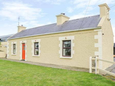 A beige cottage with three windows an orange door and a grass lawn at Glor Cottage Cahir Aghamore near Knock County Mayo