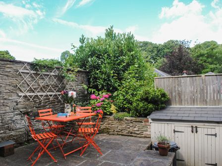 A patio with an orange metal table and chairs surrounded by plants and a stone wall at 2 Court Cottages in Aveton Gifford