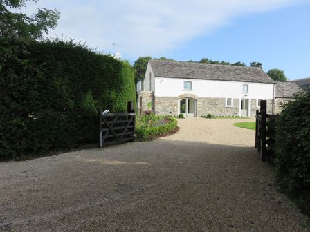 A gravel driveway leading to a stone and white house with a wooden gate and tall hedges at Old Village Barn Woodford County Galway