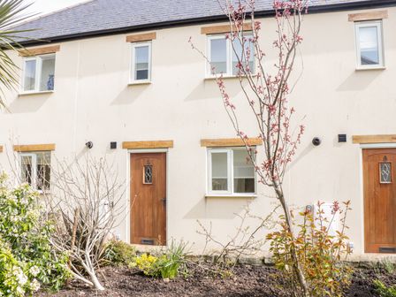 Exterior view of a beige two-story house with wooden doors and white framed windows with plants and small trees in the front garden at 9 Malthouse Court Watchet