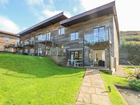 Exterior view of a modern wooden building with balconies and green lawn at Sea Breeze 17 Gannel in Porthtowan