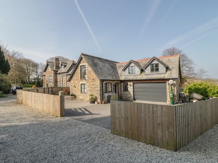 A stone house with a slate roof and a fenced driveway at The Coach House in St Columb Major