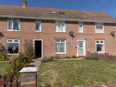 A brick terraced house with a green front door and front lawn at The Lookout -The House With A View in Weymouth