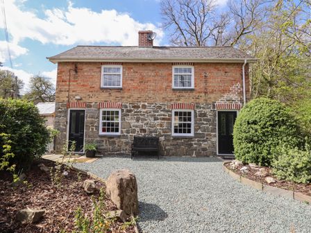 Front view of a two story stone and brick house with two black doors and four windows a bench and gravel driveway at Tan Y Capel in Machynlleth