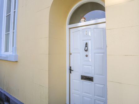 A white door with a knocker letterbox and number one on a yellow wall with an arched window above at Seion Chapel in Beaumaris