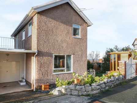 An exterior view of a two-story house with a garage and garden area bordered by stone wall at Bay View House in Colwyn Bay