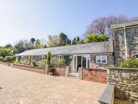 A stone and brick single-story building with a sloped roof and open door surrounded by greenery at FernGully in St Columb Major