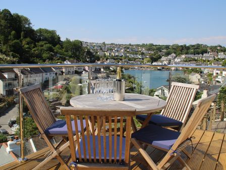 A balcony with a wooden table and four chairs with blue cushions overlooking a town and a river at Kittiwake in Noss Mayo