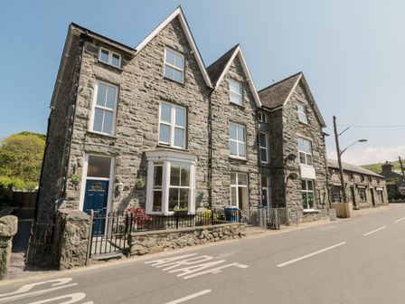 A stone building with multiple windows and blue doors along a street at Angorfa in Llanbedr