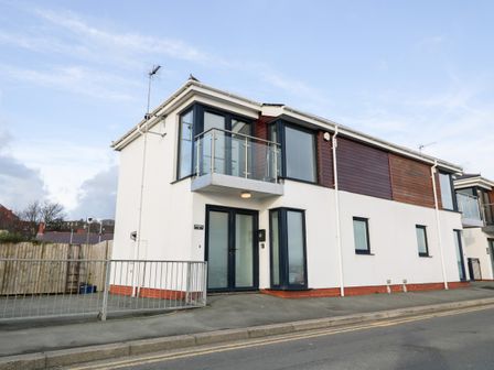 A modern two-story building with white walls and wood paneling with balconies at 8 Marina View in Pwllheli