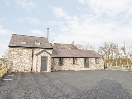 A stone exterior of a cottage with two gray doors and three windows on a paved area at Rhydau Cottage in Pentir near Deiniolen