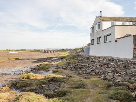 A rocky shoreline with a white building on the right and a sailboat on the left at Waterside in Ravenglass