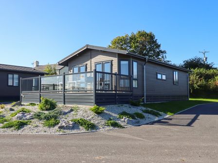 A modern single story house with a raised patio and glass railing surrounded by gravel and small plants at Ash Lodge in Teigngrace near Newton Abbot