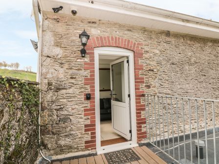 An open white door set in a stone and brick wall with a black outdoor lantern and metal railing on a wooden deck at Lower Norton Apartment in Dartmouth