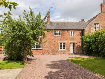 A brick house with white framed windows a gravel driveway and a tree in front at Well House Farm Flat 1 in Bretton