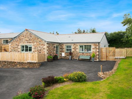 A stone cottage with a paved driveway fenced garden and flowerbeds at Be Our Guest Cottage in Chacewater near Truro