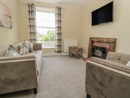 A living room with sofas a TV mounted above a fireplace and a window with curtains at Coquet View Apartment in Warkworth