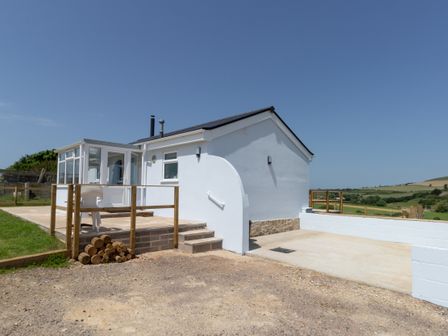 A white house with a glass porch and wooden railings on a paved patio at Village View in Burton Bradstock