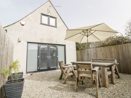 A small outdoor patio with wooden table and chairs and an umbrella at Lily Cottage in Camelford