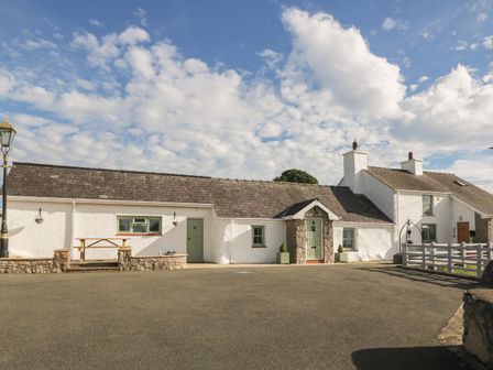 A white cottage with green doors and windows and a wooden bench outside at Buarthau Cottage in Llanrug