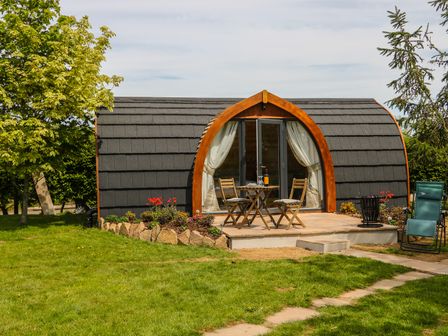 Small pod structure with curved roof and wooden frame doors with outdoor table and chairs on patio at Chapel Pod in Callington