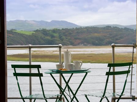 A balcony with a green metal table and two chairs overlooking a river and hills at Aber Wharf Porthmadog
