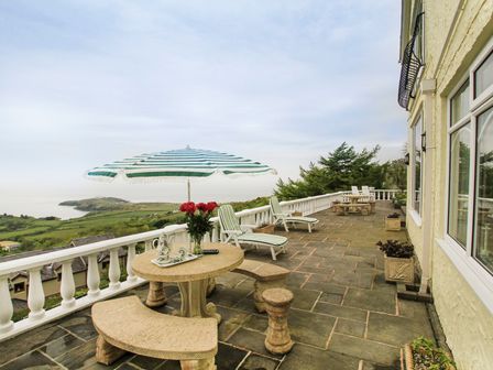A stone patio with tables benches and umbrellas overlooking a coastal landscape at Amolca in Llaneilian