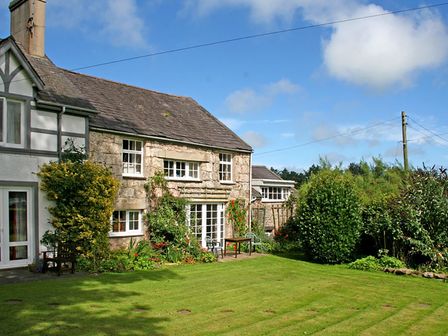 A stone and white house with garden furniture and plants on a lawn at Foel Stable Cottage in Brynsiencyn