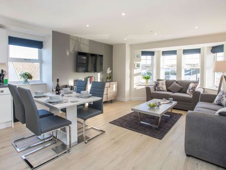 A living room and dining area with gray sofas and chairs a wall-mounted TV and a coffee table at Beach Lookout in Benllech