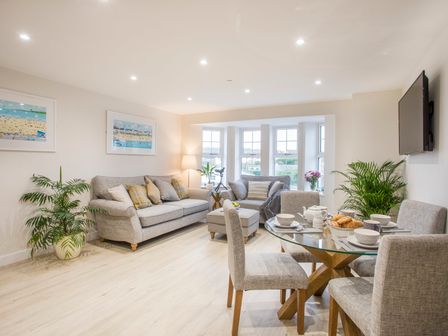 A living room with grey sofas a glass dining table with chairs and indoor plants at The Beach Pad in Benllech