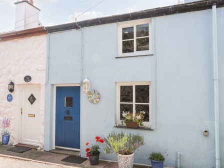 A light blue cottage exterior with a blue door numbered 72 and window boxes with flowers at Blue Cottage in Beaumaris