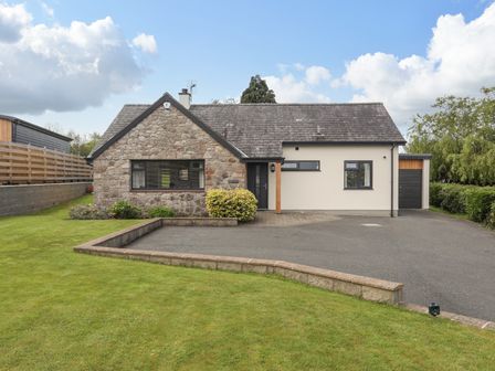 A stone and white exterior house with a driveway and a green lawn at Bronallt in Y Felinheli