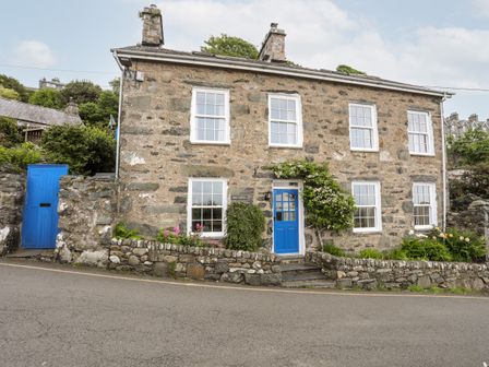A stone cottage with blue doors and white window frames with a stone wall and plants at Bron Castell in Harlech
