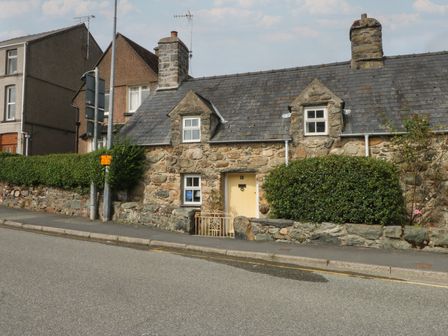 A stone house with a hedge and gate on the street at Y Bwthyn in Criccieth