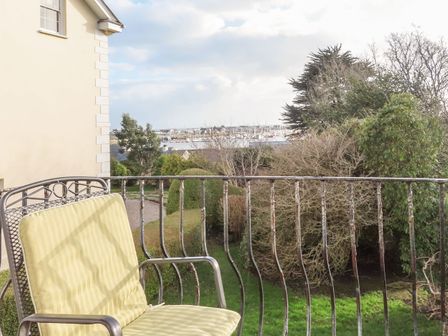 A balcony with a metal chair overlooking a garden and marina at Bwthyn at Brynhyfryd in Pwllheli