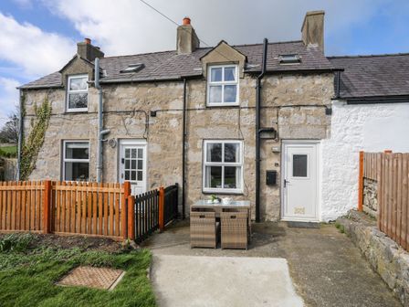 Stone cottage exterior with two white doors patio table and chairs and wooden fences at Cae Person in Llangoed