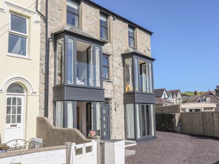 The exterior of a stone building with two glass balconies and a fenced driveway at Cambrian House in Criccieth