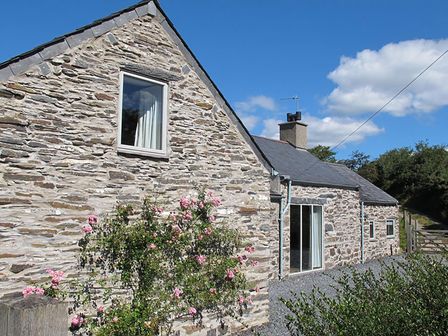 An exterior view of a stone house with windows and a chimney surrounded by plants and a gravel pathway at Cefn Isaf in Porthmadog