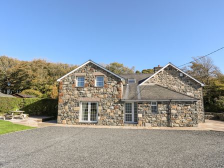 A stone house with two gable ends and glass doors with a gravel driveway and picnic table at Cennin in Criccieth