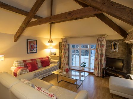 A living room with exposed wooden beams sofas a glass coffee table and a TV at The Coach House - Beaumaris
