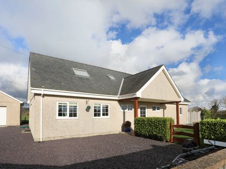 A house with beige walls and a dark roof with skylights a gravel driveway a small green hedge and a wooden gate at Dwyros in Pwllheli