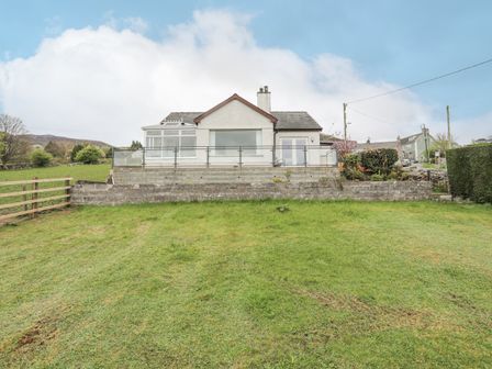 A house with a lawn and a stone retaining wall with railing at Frondeg in Rhiwlas